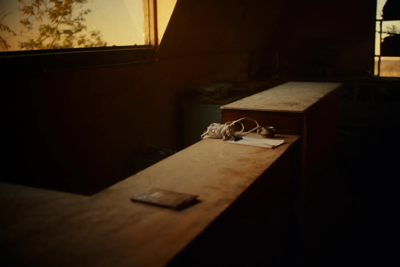 A small business back office before opening: a worn desk, a clipboard, a coiled cable and a closed ledger in low morning sun.